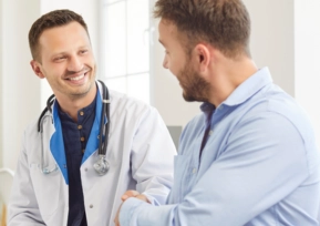 Médico sorridente cumprimenta paciente durante atendimento em consultório, transmitindo confiança e acolhimento.