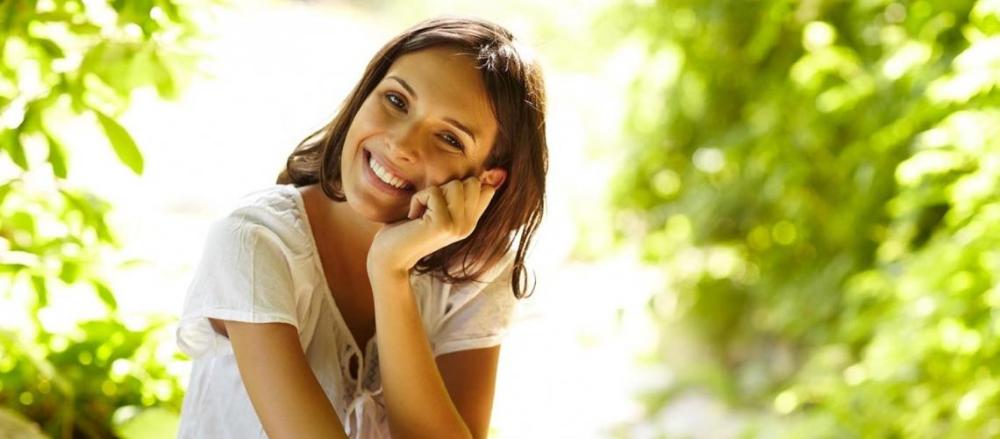 Mulher sorrindo próximo a algumas folhagens verdes