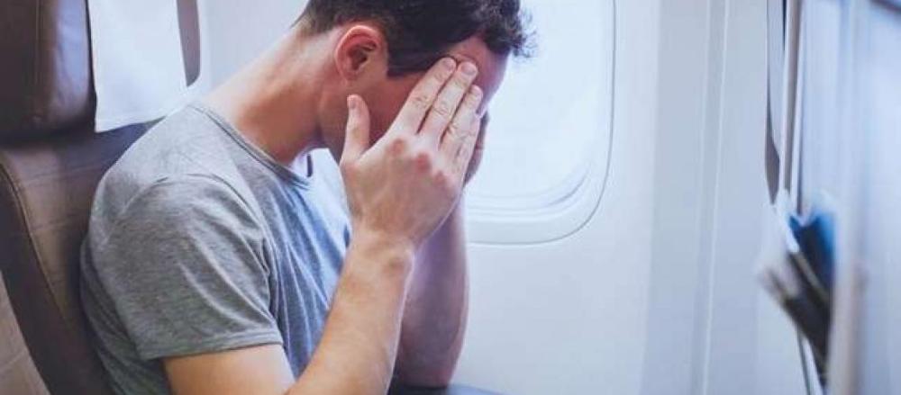 Homem dentro de um avião com a mão nas têmporas, indicando preocupação