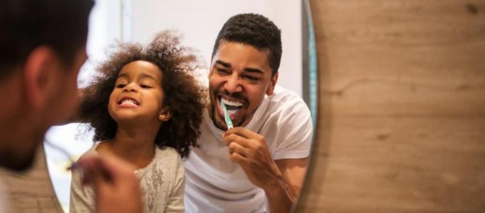 Homem e criança escovando os dentes juntos e sorrindo