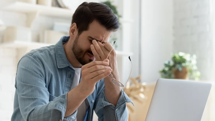 Homem com a mão nos olhos e o óculos na mão
