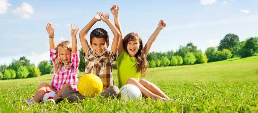 3 crianças com as mãos levantadas, brincando na grama