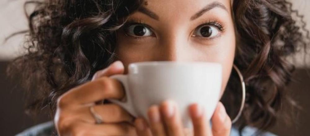 Mulher segurando uma xícara de café na frente da boca