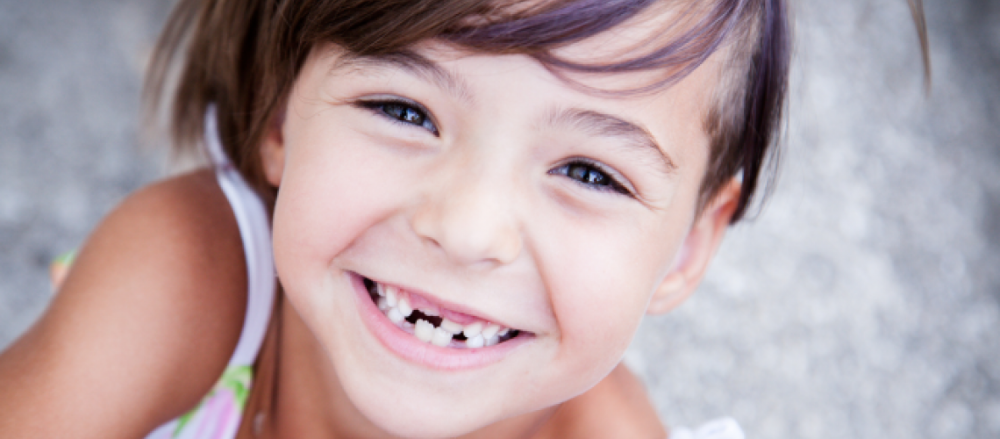 Criança sorrindo, com alguns dentes permanentes nascendo