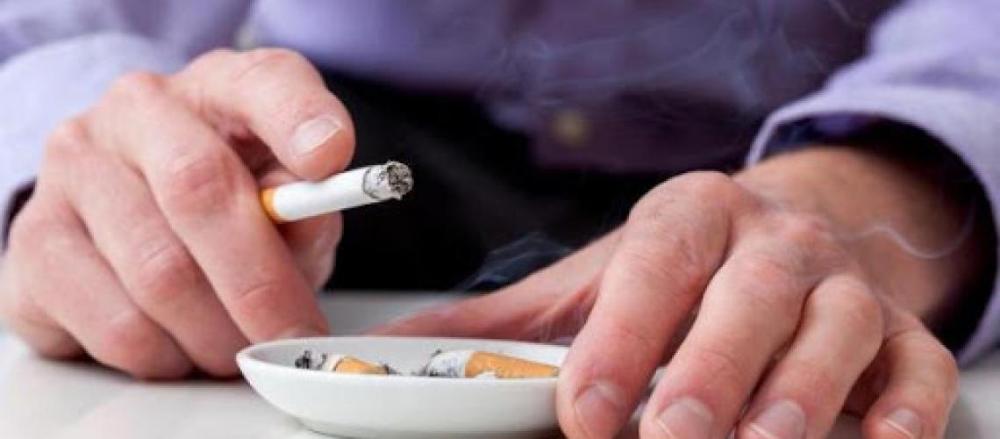 Uma pessoa com cigarro acesso na mão, encima de um cinzeiro
