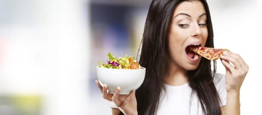 Mulher sgurando um pote de salada enquanto come pizza