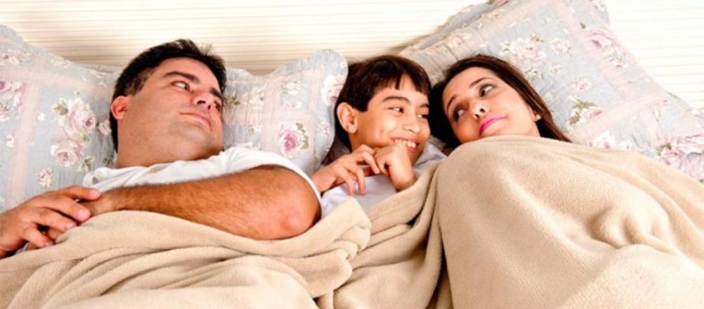 Casal deitado na cama, com o filho rindo deitado entre eles