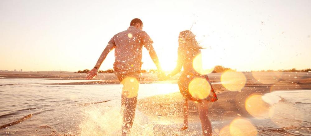 Casal de mãos dadas, correndo na beira do mar