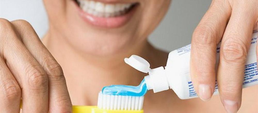 Mulher sorrindo enquanto coloca pasta de dente em sua escova
