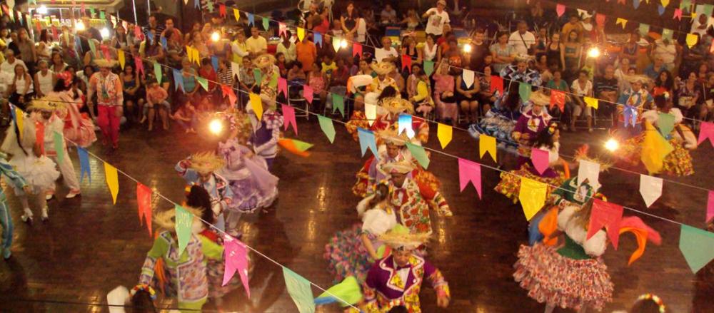 Pessoas com roupas de festa junina em um evento, com decoração temática