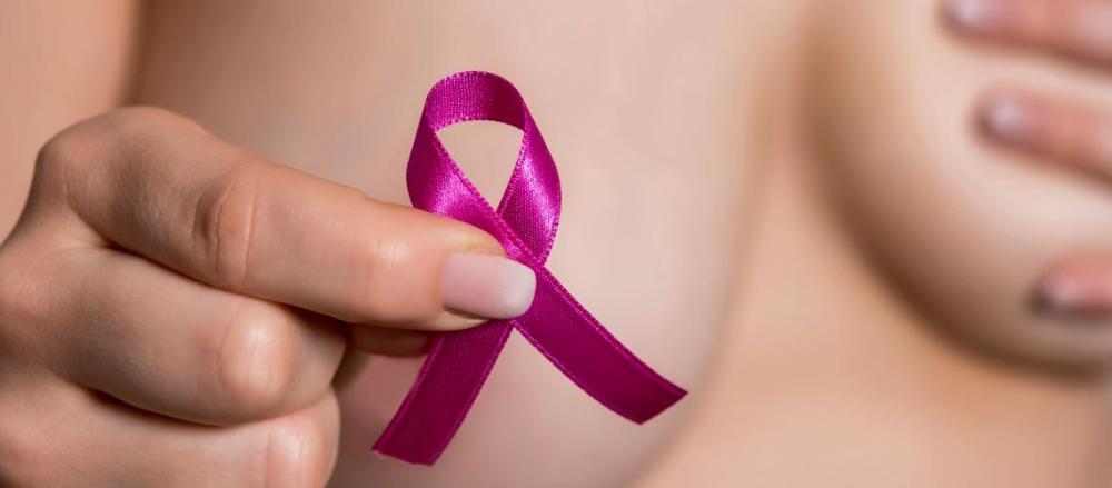 Mulher cobrindo os seios com as mãos e segurando um fita rosa, relacionada ao outubro rosa