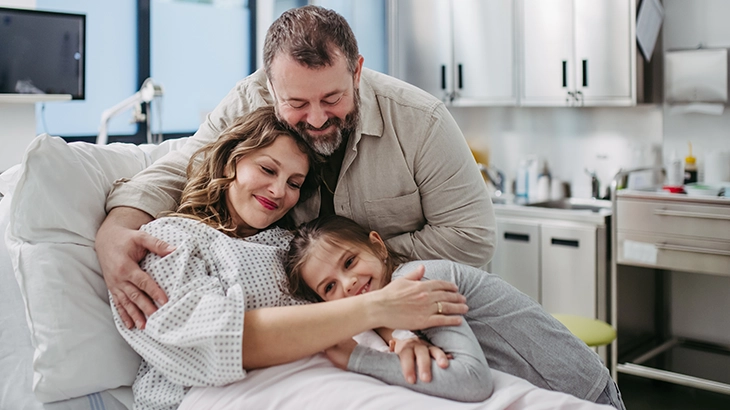 Familia se abraçando feliz no leito de uum hospital.