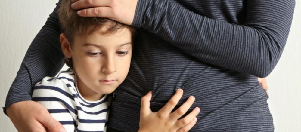 Menino abraçado na mãe, com expressão triste