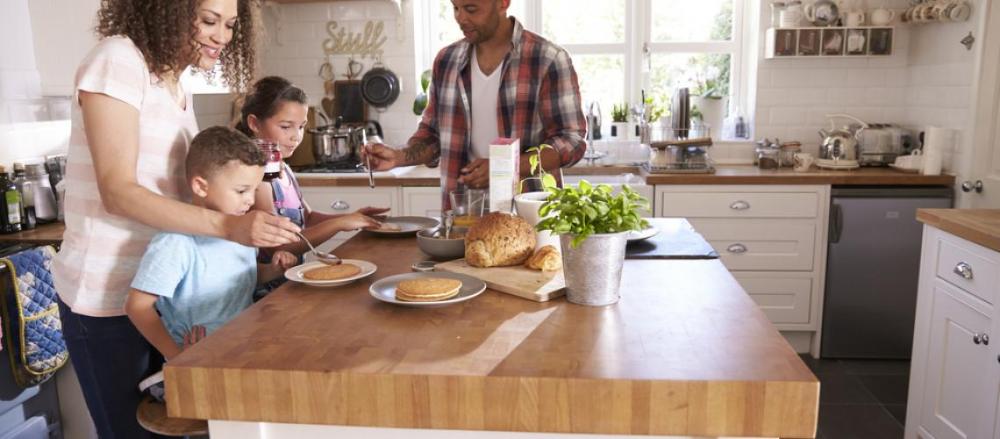 Casal com dois filhos na cozinha preparando o café da manhã
