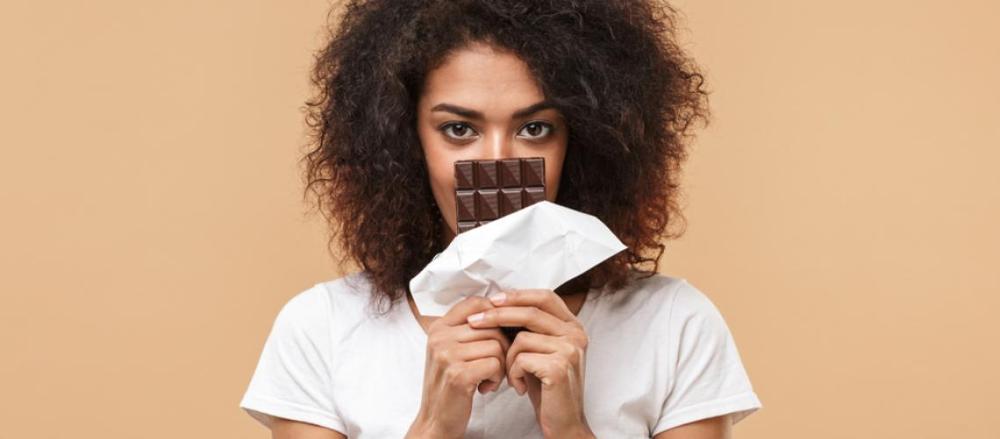 Mulher cobrindo a boca com uma barra de chocolate