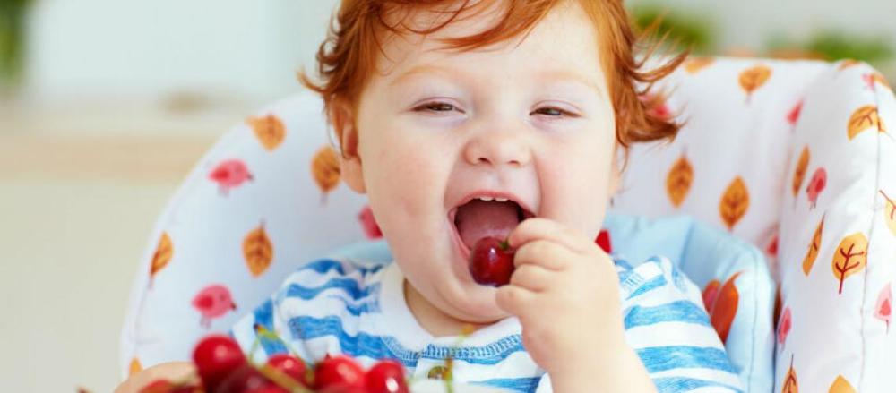 Bebê sorrindo e comendo cereja
