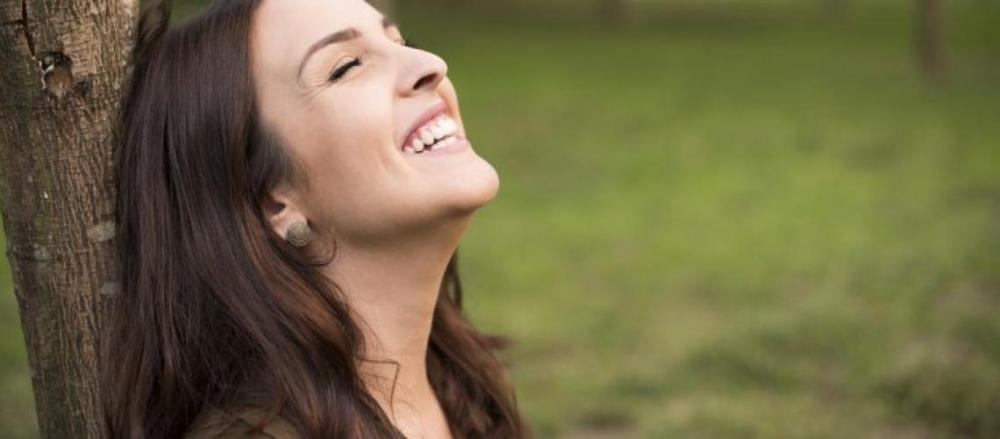 Mulher sorrindo, encostada no tronco de uma árvore