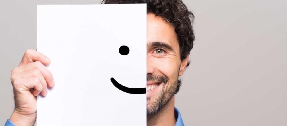 Homem sorrindo, segurando uma folha com um sorriso desenhado na metade do rosto