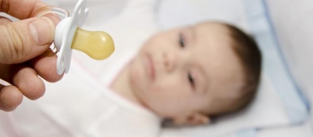 Uma chupeta em destaque, com um bebê ao fundo