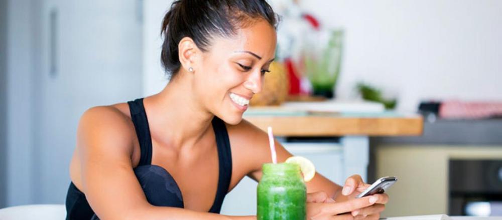 Mulher tomando suco verde enquanto usa o celular