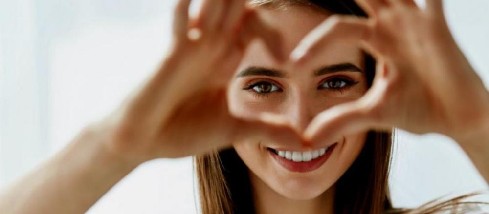 Mulher sorrindo e fazendo sinal de coração com os dedos das mãos
