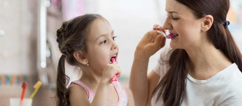 Imagem de uma mulher e uma criança escovando os dentes juntas