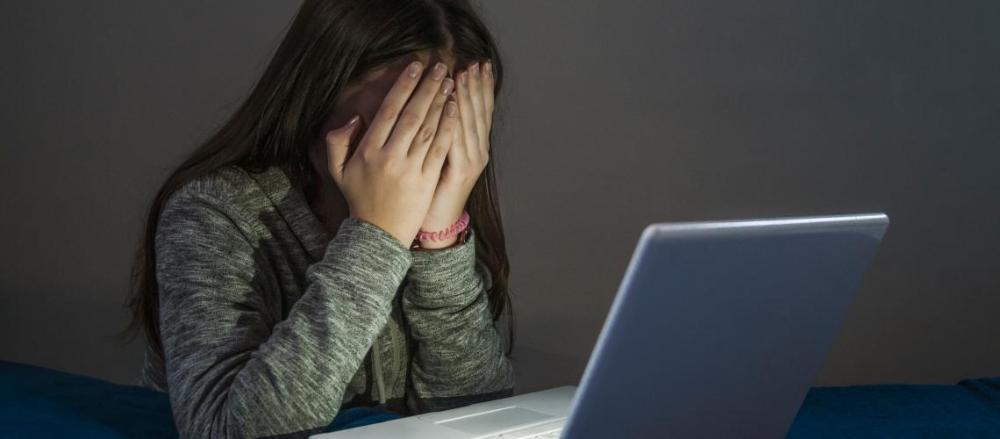 Criança na frente do computador cobrindo os olhos