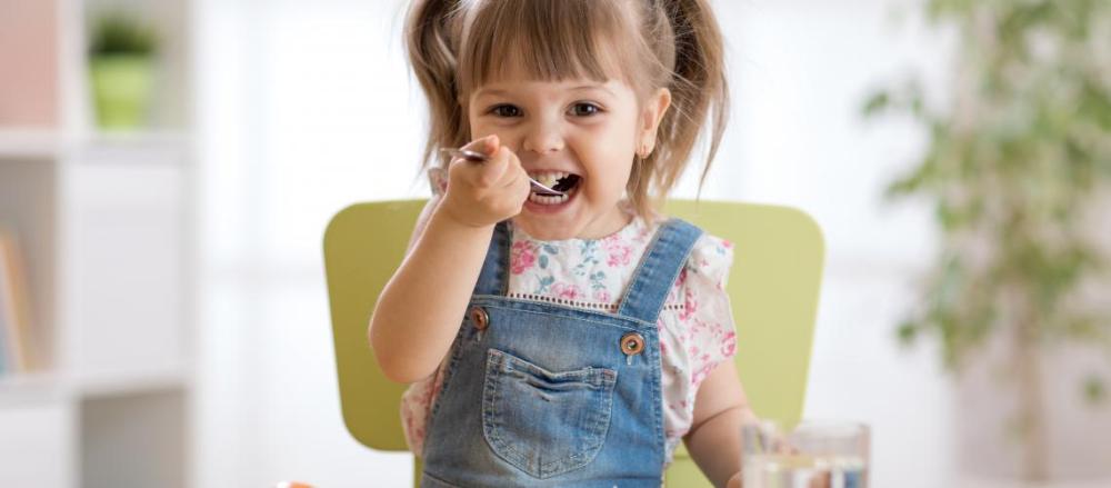 Criança pequena sorrindo com colher na boca