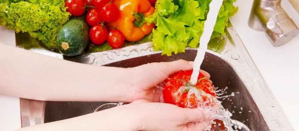 Mulher higienizando alimentos naturais na pia