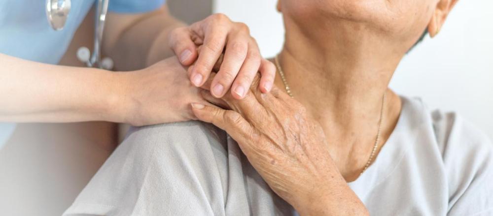 Mulher sentaada, com enfermeita levando as mãos aos seus ombros