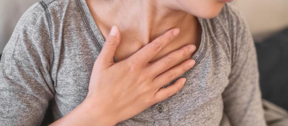 Mulher com a mão entre o peito e a garganta, indicando possível problema respiratório