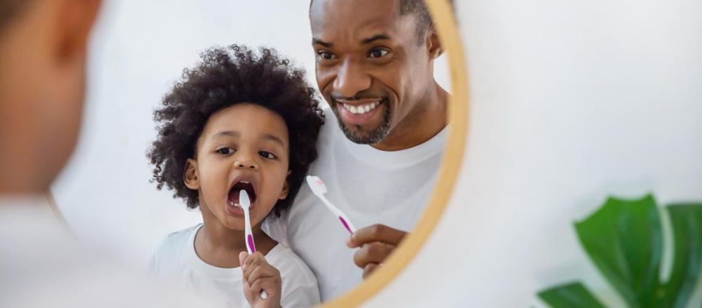 Pai e filho escovando os dentes na frente do espelho