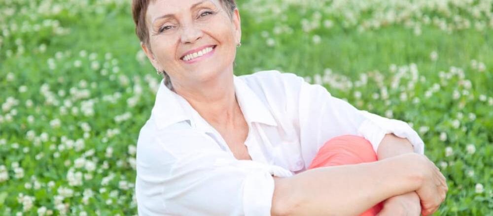 Mulher acima dos 40 anos sentada na grama e sorrindo