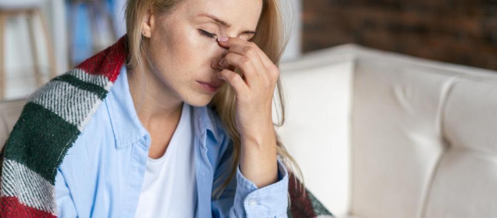 Mulher de olhos fechados, apertando a ponte do nariz, com um cobertor nos ombros