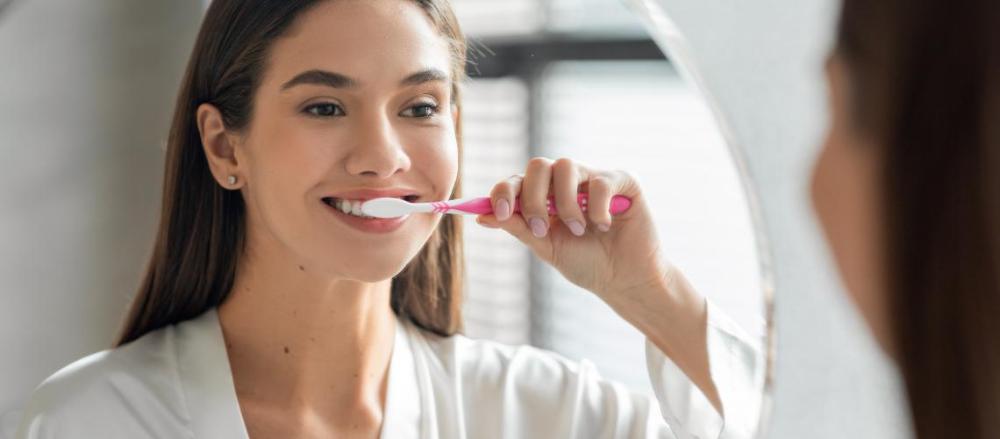 Mulher escovando os dentes de frente para um espelho