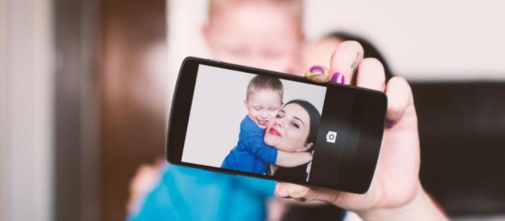 Mulher segurando um bebê e tirando uma selfie dos dois com o celular