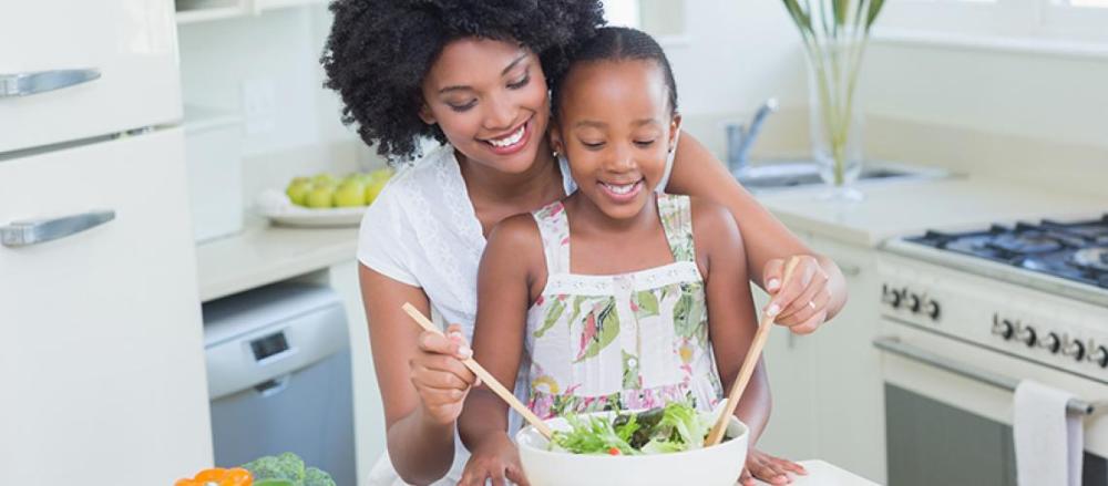 Mulher adulta e uma criança preparando uma salada, felizes
