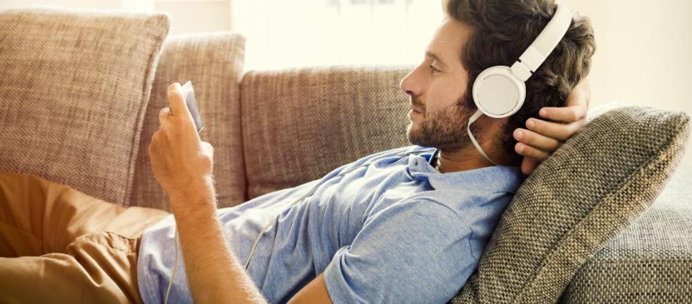 Homem deitando com fone de ouvindo enquanto usa o celular