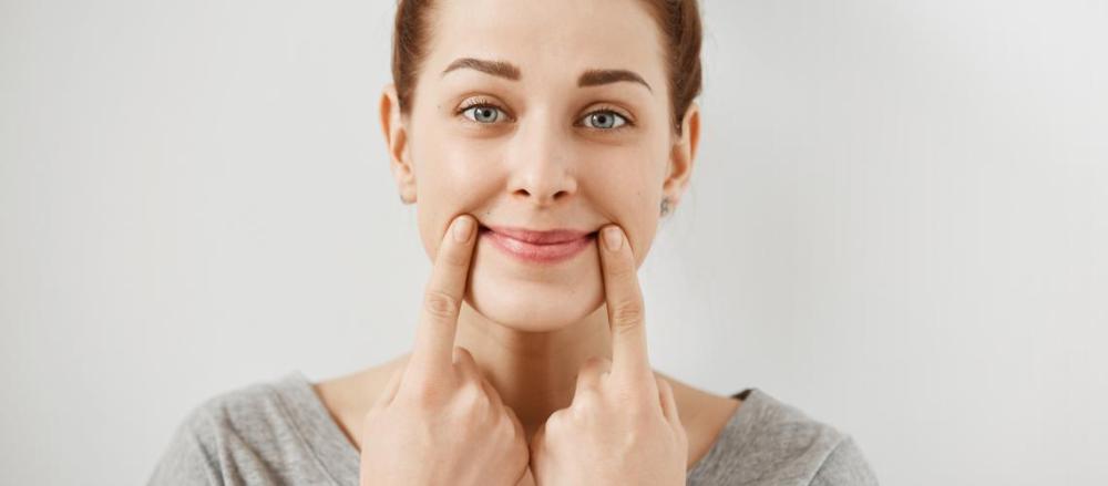 Uma mulher forçando um sorriso com os dedos na boca