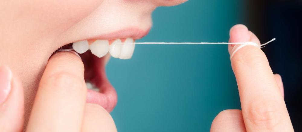 Mulher usando fio dental para limpeza dos dentes