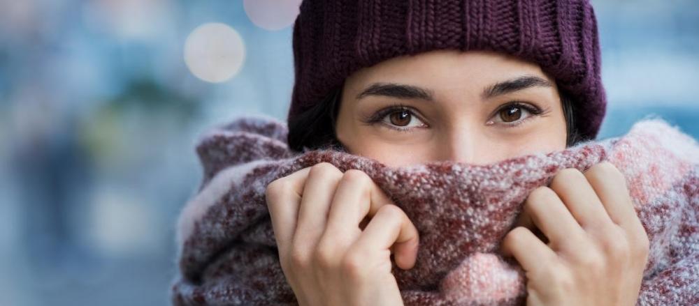 Mulher com o orsto encoberto por um cachecol enquanto usa um gorro