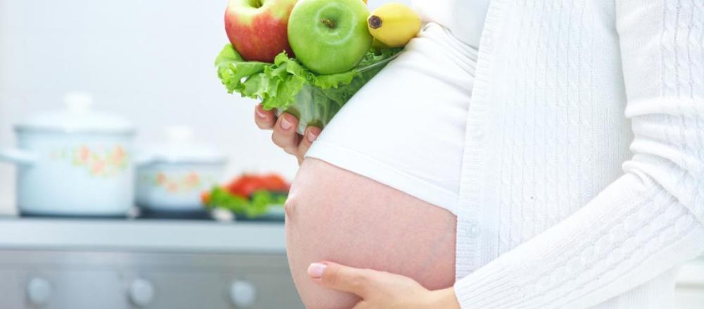 Mulher grávida com a mão na barriga enquanto segura algumas verduras