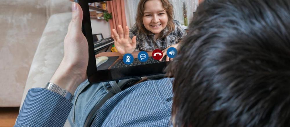 Homem deitado olhando um tablete, em um conversa por videochamada com outra pessoa