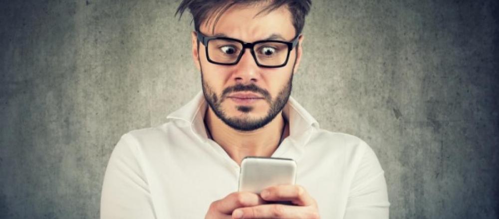 Homem espantado enquanto olha para o celular