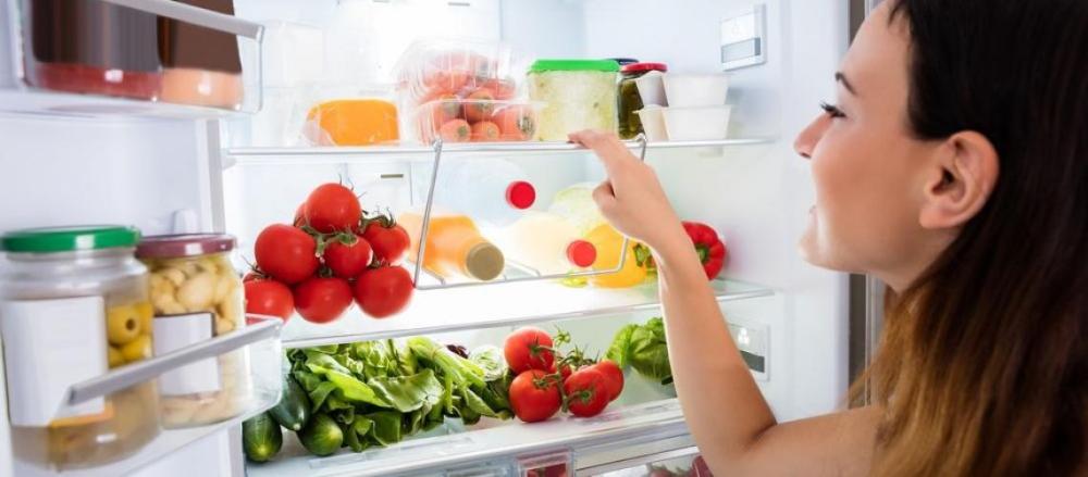 Mulher em frente a uma geladeira com frutas, elgumes e verduras