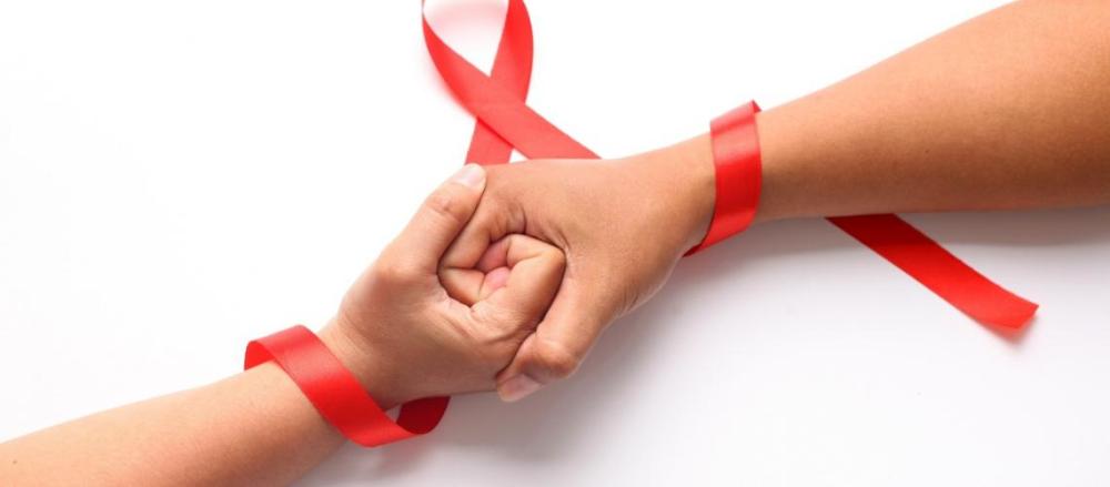 Duas pessoas de mãos dadas com uma fita vermelha entrelaçando elas, em alusão ao dezembro vermelho