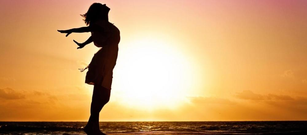 Sombra feminina de braços abertos no pôr do sol, indicando liberdade