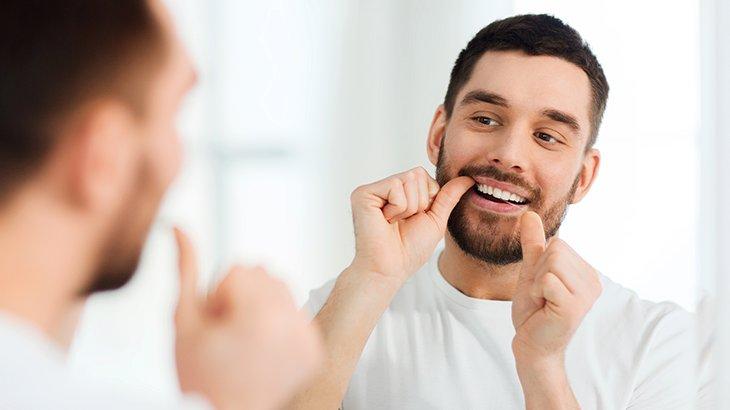 Imagem de um homem usando fio dental em frente ao espelho