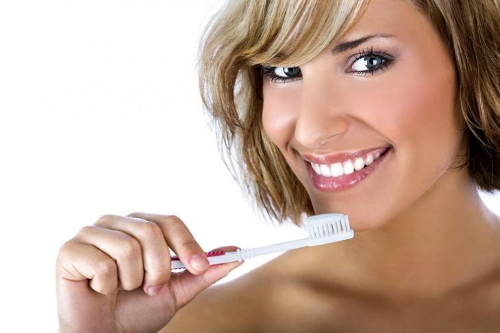 Imagem de uma mulher sorrindo enquanto leva uma escova de dentes à boca