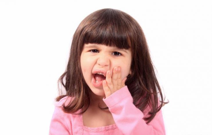 Imagem de uma criança com dor, segurando a bochecha, indicando possível dor de dente ou sensibilidade bucal
